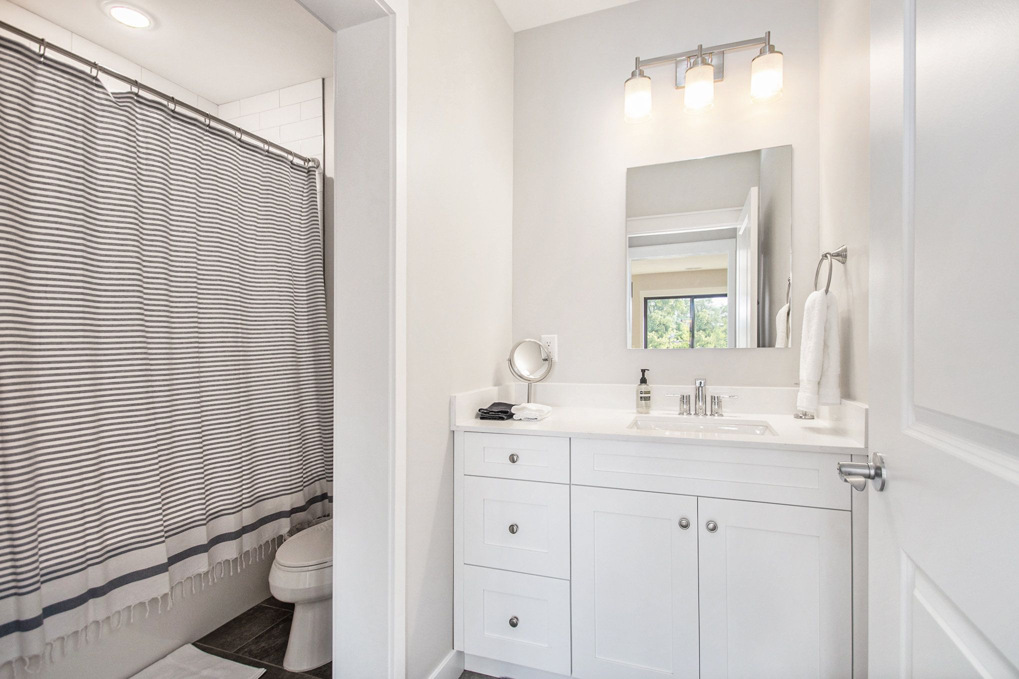 Une salle de bain avec un rideau de douche à rayures, un lavabo blanc avec un miroir au-dessus, et des toilettes.