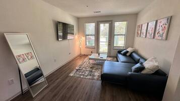 A modern living room with a black leather sofa, a coffee table, a floor lamp, and a large mirror.