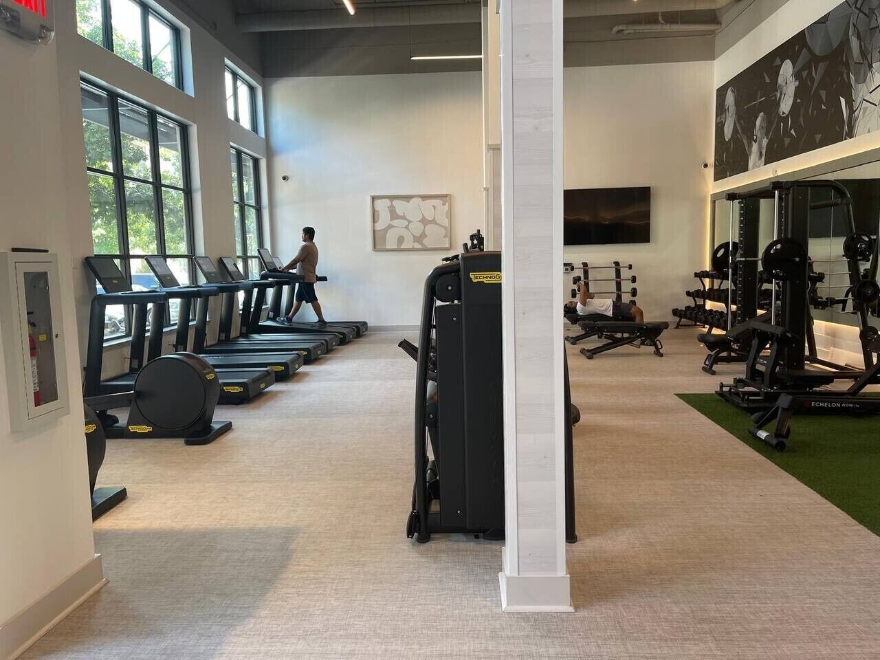 Une salle de sport équipée de tapis de course, d’appareils de musculation et où une personne se promène.
