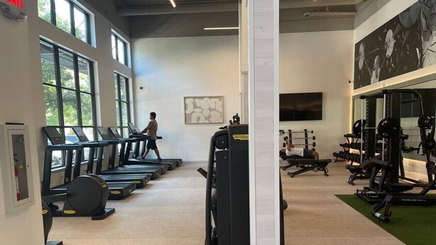 Ein Fitnessstudio mit Laufbändern, Kraftgeräten und einer Person, die geht.