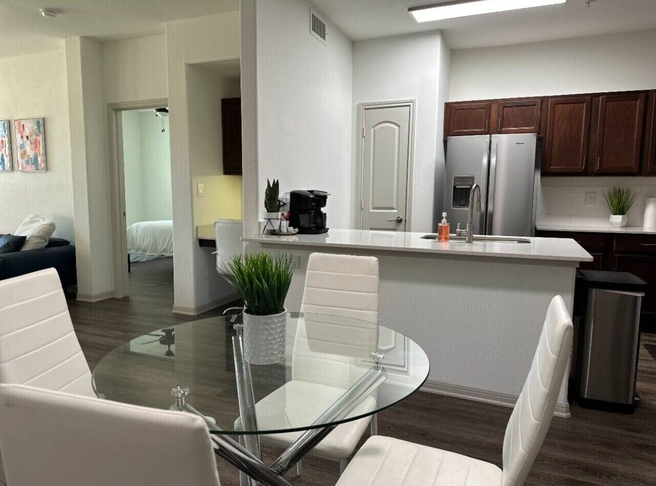 A modern kitchen with a central island, stainless steel appliances, and a dining area with a glass table.