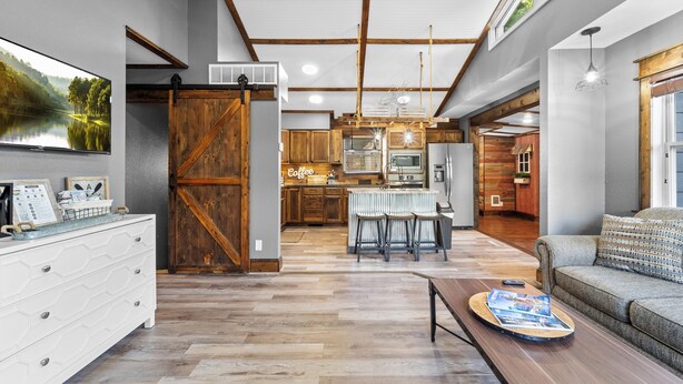 Amplia sala de estar con un televisor grande, muebles de madera, una cocina al fondo y un rincón de descanso acogedor.