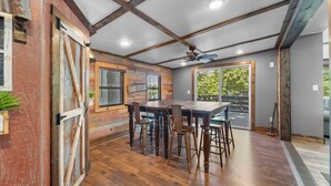 Un comedor con mesa y sillas de madera, un ventilador de techo y vistas al exterior.