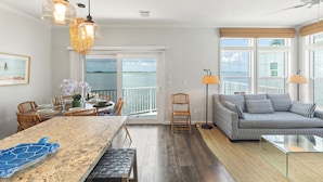 A spacious living area with a large window, a sofa, a dining table, and a kitchen area. - Oceanfront 2BR Retreat - 35' Dock, Sunrise Views, Boater's Paradise (Cudjoe Key)