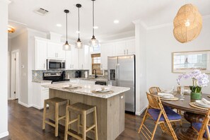 A modern kitchen with white cabinetry, a central island with stools, and a dining area with wicker chairs.