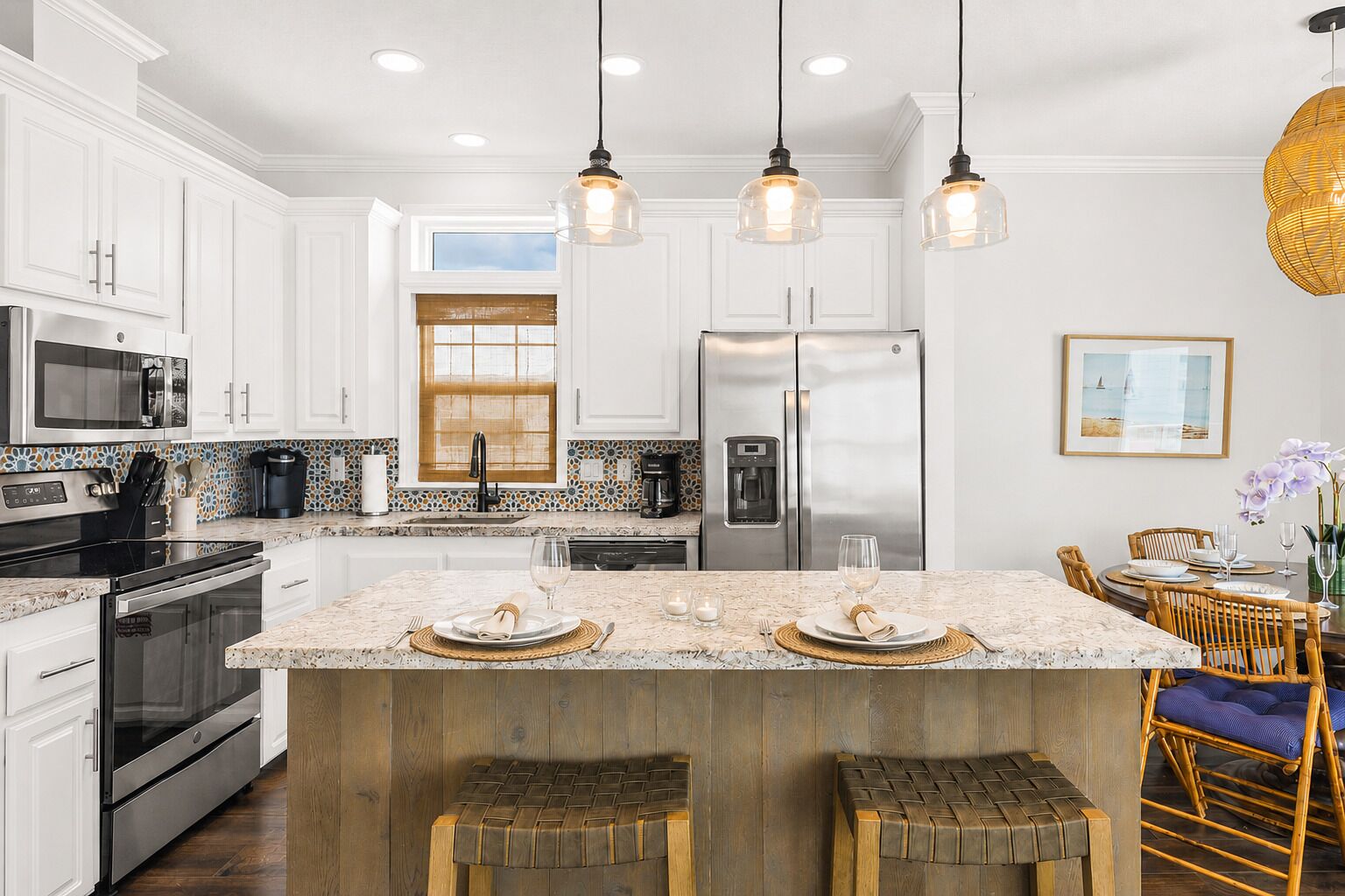A modern kitchen with white cabinets, stainless steel appliances, a large island with stools, and pendant lighting.