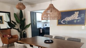 Un comedor con una mesa de madera, sillas tapizadas en gris, una lámpara colgante tejida y un cuadro de un leopardo en la pared.
