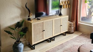Sala de estar con televisor sobre un mueble de madera, planta en maceta, lámpara colgante y vista a través de una ventana.