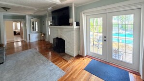 A spacious living room with hardwood floors, a fireplace, and a large sliding glass door leading to an outdoor area. - Private Beach Cottage Compound • Steps to Sand (Indian Rocks Beach)