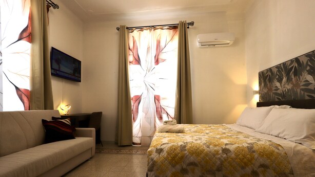 A hotel room with a bed, a sofa, a TV, and an air conditioning unit. - Alex's House La Spezia Migliarina 10 min from Migliarina Station (La Spezia)