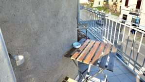 A balcony with a metal railing, a concrete wall, and a wooden table with a bowl. - Alex's House La Spezia Migliarina 10 min from Migliarina Station (La Spezia)