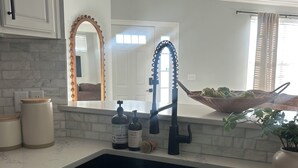 Una cocina con un lavamanos doble, armarios blancos, encimera de mármol y un espejo grande con marco decorativo.