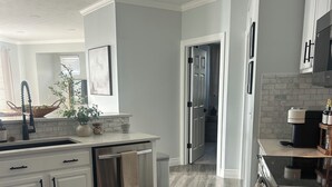 Una cocina moderna con armarios blancos, lavavajillas de acero inoxidable y piso de madera.