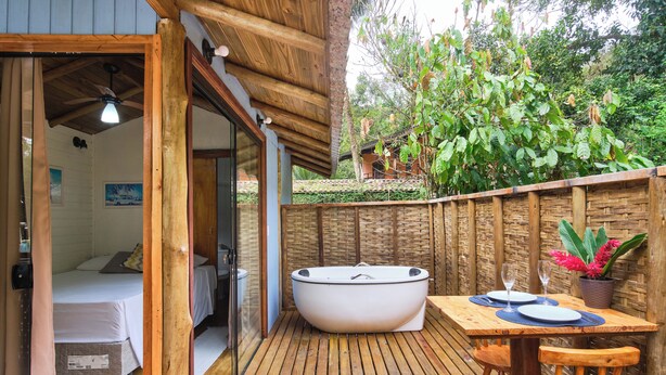 A wooden deck with a hot tub, a table with two glasses, and a bed in a room.