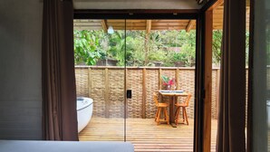 A room with a wooden floor, a bed, a table with chairs, and a view of a garden through a glass door.