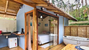 A room with a bed, a small kitchenette, a bathtub, and a dining table with a glass.