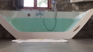 A bathtub with a faucet and showerhead, a window with curtains, and patterned tiles on the walls.