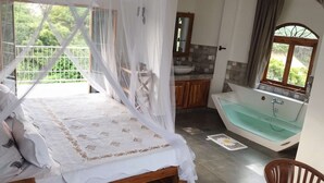 A bedroom with a bed, a bathroom with a bathtub, and a view of greenery.