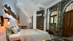 A bedroom with a bed, bedside table, lamp, and a stone wall.