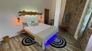 A bedroom with a bed, two wall-mounted lights, a wooden headboard, a small table, and a stone wall.