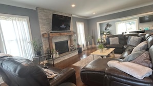 Una sala de estar con chimenea, sofás de cuero, televisor y una pared decorativa de piedra.