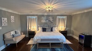 Un dormitorio con una cama grande, dos mesitas de noche con lámparas, un banco, un sofá y una lámpara del techo.