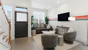 Un salon moderne comprenant un canapé, deux fauteuils, une table basse et un téléviseur fixé au mur.
