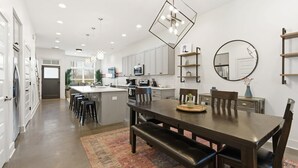 Une cuisine moderne avec des meubles blancs, un îlot central et un coin repas comprenant une table et des chaises en bois.