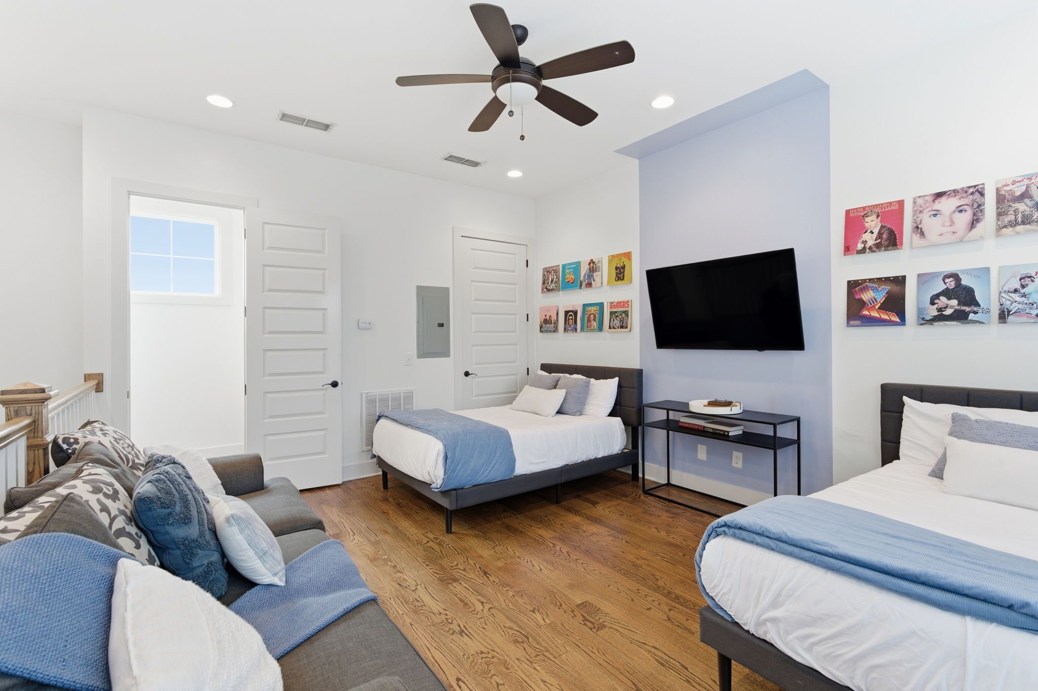 A modern bedroom with two beds, a ceiling fan, a TV, and wall art.