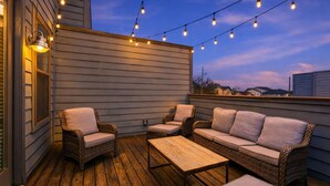 Une terrasse extérieure aménagée avec des meubles en osier, des guirlandes lumineuses et une plateforme en bois.