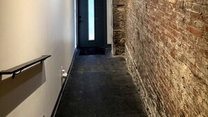 En hall med en tegelvägg, en dörr längst ner och en modern lampa med sfäriska element.