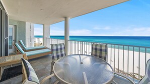 Ein Balkon mit Glastisch und Korbstühlen, mit Blick auf einen Strand.
