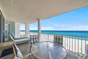 A balcony with a glass table and wicker chairs, overlooking a beach. - 2BR Beachfront Condo Long Beach Resort 6th Floor On Site Snack Bar (Panama City Beach)