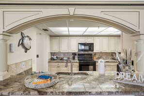 A kitchen with a marble countertop, a large island, and a view of the living area through an arched doorway. - 2BR Beachfront Condo Long Beach Resort 6th Floor On Site Snack Bar (Panama City Beach)