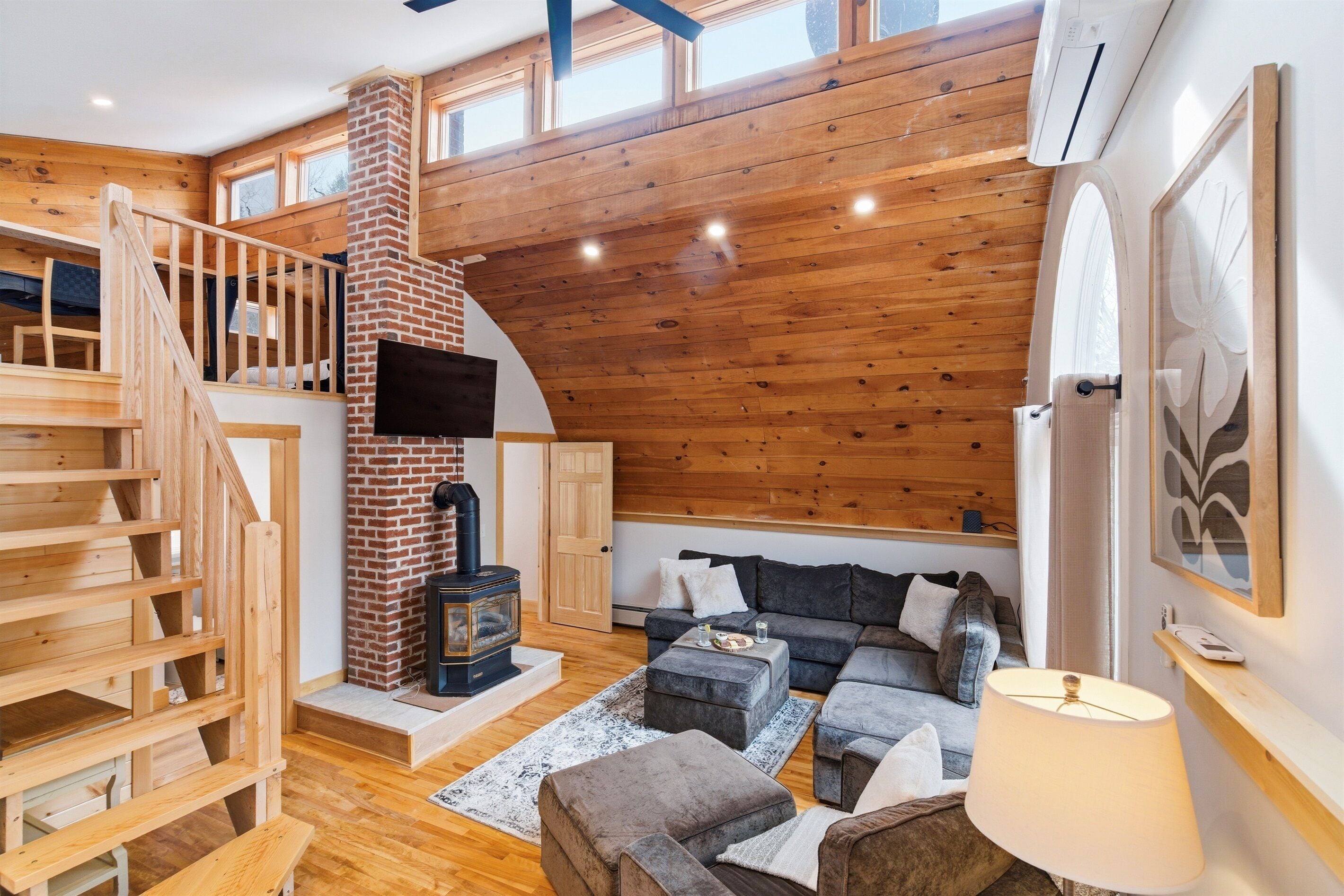 Een kamer in loftstijl met een houten trap, een open haard, een bank en een televisie.