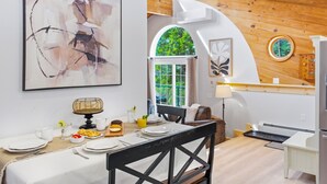 Un comedor con una mesa dispuesta para dos, un cuadro abstracto grande y vistas al exterior a través de una ventana.
