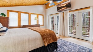 Un dormitorio con cama, techo de madera, ventanas grandes y puerta corrediza de vidrio.