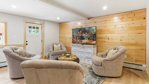 Una sala de estar con tres sillones beiges, una pared de madera, un televisor y un mueble blanco.