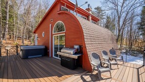Una cabaña roja con terraza, jacuzzi y parrilla.