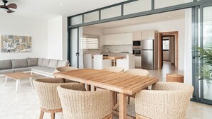 A modern living room with a sofa, a dining table with chairs, and a kitchen area visible through an open door. - Penthouse 3BR Ocean View & Pool | Sol de Arena F7 (Las Terrenas)