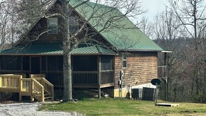 Une cabane en bois avec un toit vert, une terrasse en bois et une allée gravillonnée.