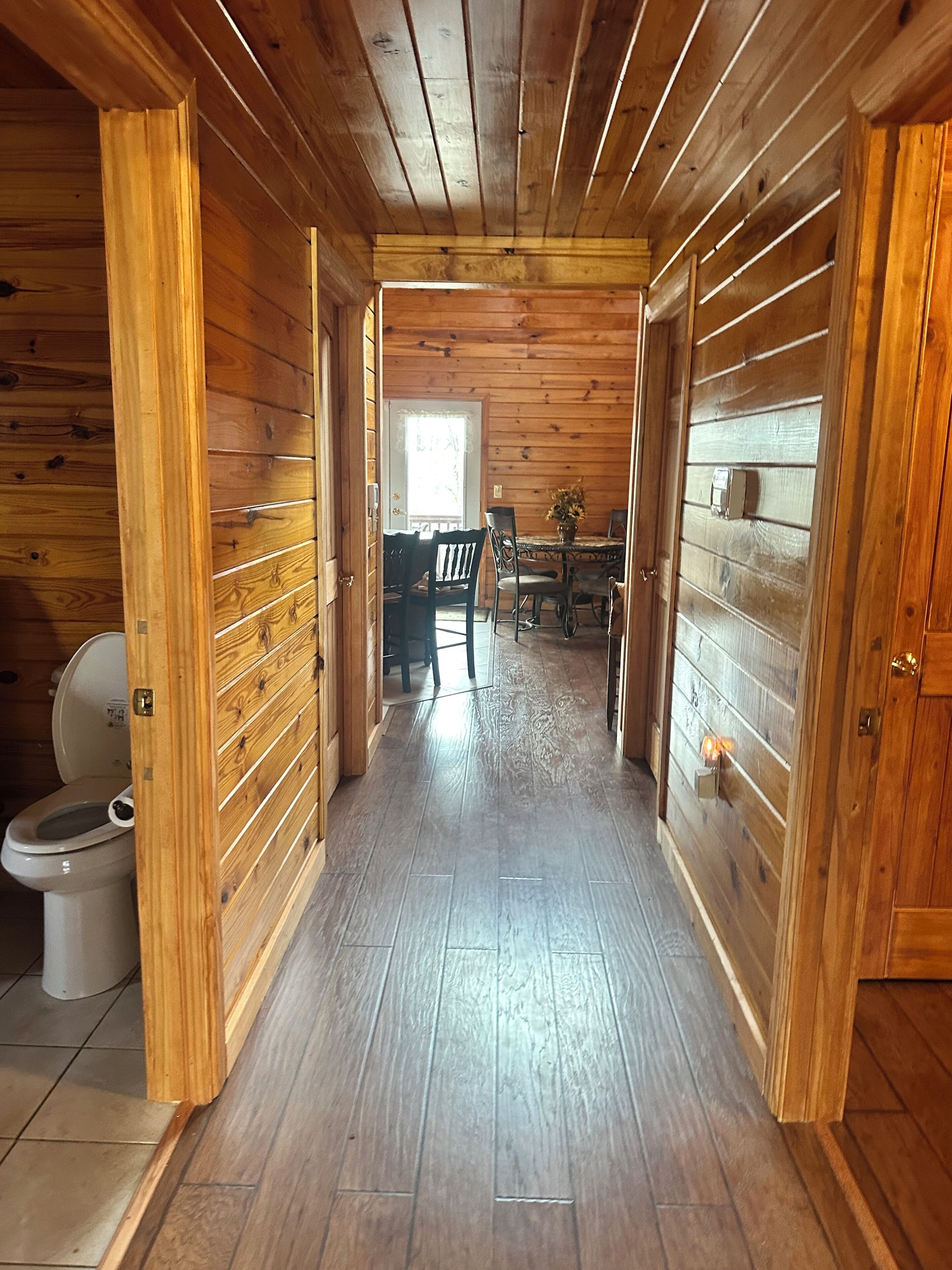 Un intérieur en bois avec un couloir menant à une salle à manger, des toilettes visibles et une porte dotée d’un interrupteur.