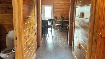 Un intérieur en bois avec un couloir menant à une salle à manger, des toilettes visibles et une porte dotée d’un interrupteur.