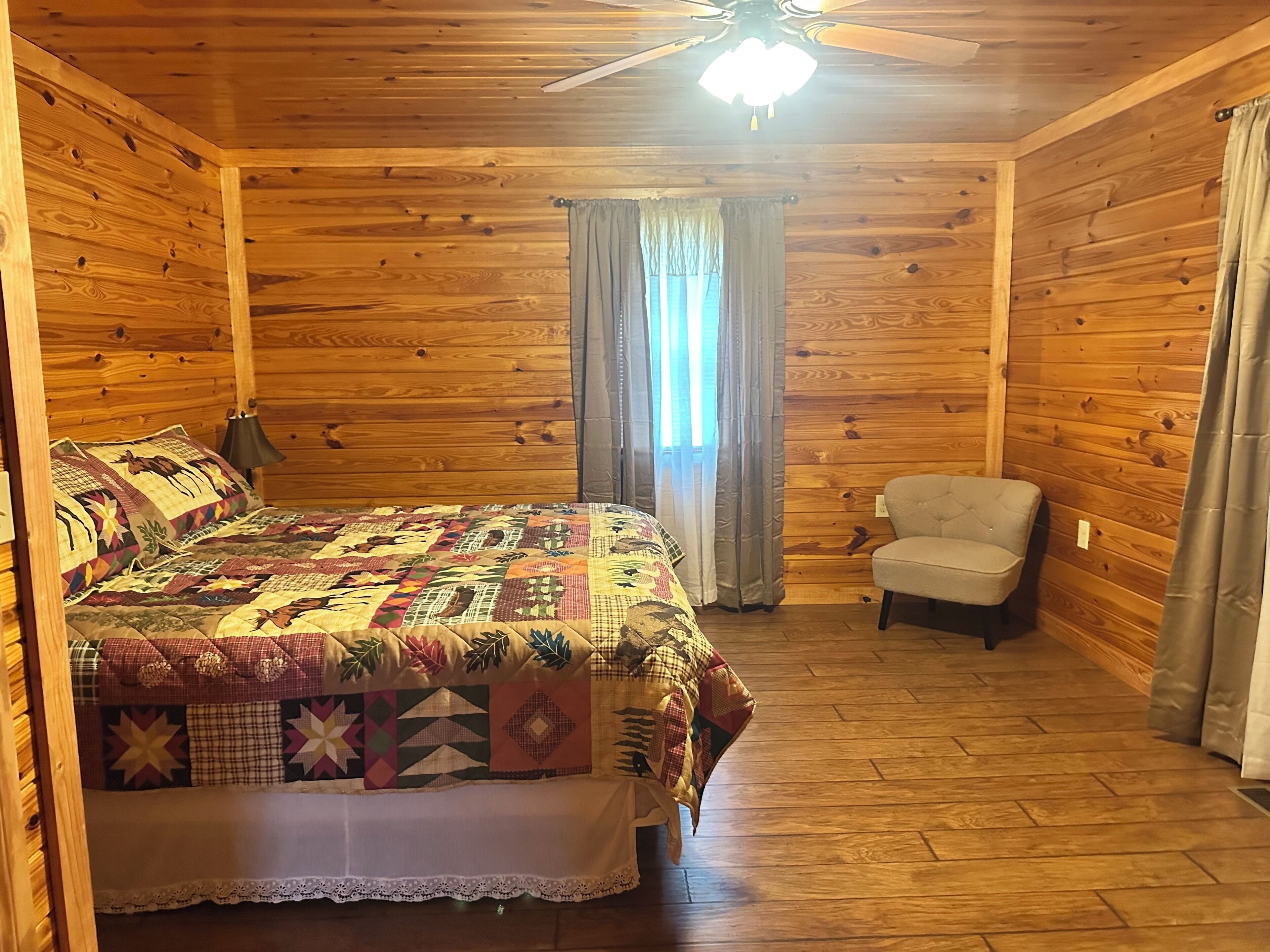 Dormitorio de cabaña de madera con cama, silla y ventilador de techo.