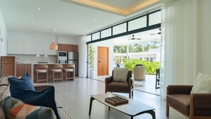 Un grand espace de vie comprenant un canapé, des fauteuils, une table basse et une cuisine à l’arrière-plan.
