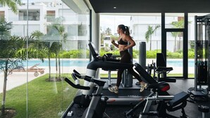 Ein Fitnessstudio mit Laufbändern, Kraftgeräten und Blick auf ein Schwimmbecken und Grünflächen.