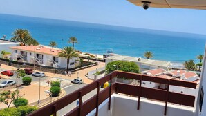 Ein Balkon mit Blick auf das Meer, Gebäude und eine Straße mit Autos.