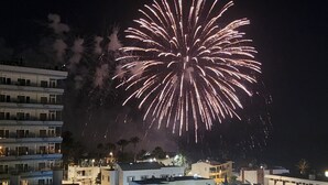 Ein Gebäude mit mehreren Etagen und Balkonen, ein klarer Nachthimmel und Feuerwerk im Hintergrund.