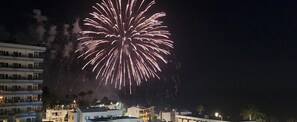 A building with multiple floors and balconies, a clear night sky, and fireworks in the background. - English Beach: Apartment next to the Ocean. (San Bartolomé de Tirajana)