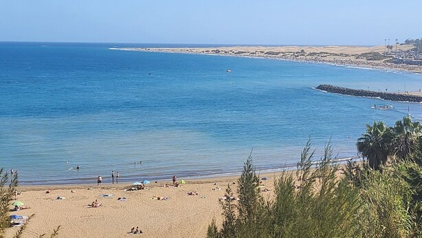 Ein Strand mit klarem, blauem Wasser, sandigem Ufer und einer weiter entfernten Skyline.